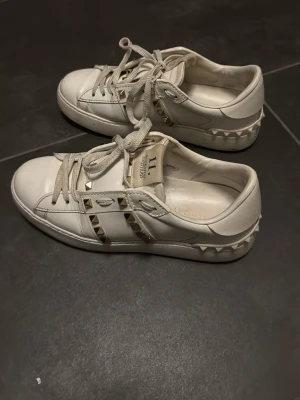 Vita Valentino sneakers med nitar - Säljer ett par vita sneakers från Valentino med coola guldfärgade nitar längs sidorna. Skorna köptes för 1 vecka sedan och är inte andvända sen dess då det är fel storlek!💕storlek 35