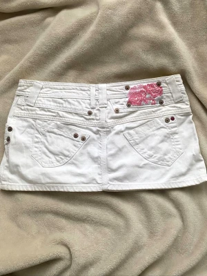 Vit minikjol med rosa detalj - Vit kjol lågmidjad med rosa detaljer 🤍🤍💕midjemått 39 cm  men sitter mer på höfterna, längd 28 cm