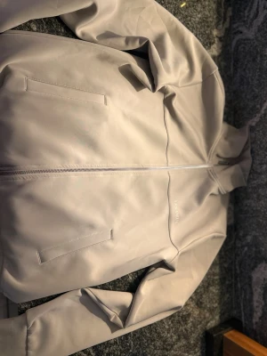 Beige ziptröja från Les Deux - Snygg beige ziptröja från Les Deux med hög krage och diskret logga på bröstet. Tröjan har långa ärmar, ribbade muddar och två fickor framtill. Perfekt för en clean och stilren look.