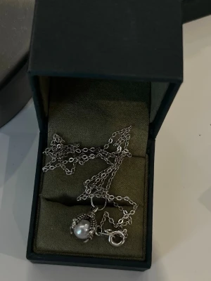 Silverhalsband med en klo/pärl berlock  - Säljer ett stilrent silverhalsband med en. rund vit pärla som hängsmycke. Kedjan är tunn och elegant, och pärlan ramas in av en detaljerad silverinfattning } Perfekt för dig som gillar klassiska smycken med en modern twist. Antingen rosfrittstål eller äkta silver.