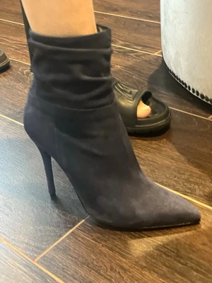 Marinblå  stövletter med smal klack - Snygga marinblå stövletter i mockaimitation med spetsig tå och hög smal klack. Dragkedja på insidan för enkel påtagning och rynkad detalj vid skaftet. Perfekta för att lyfta din outfit.