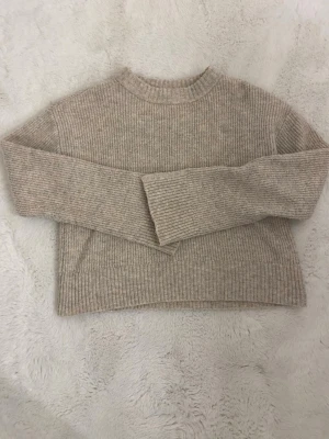 Beige ribbstickad tröja - Säljer en beige ribbstickad  tröja med långa ärmar och slits   Tröjan har en rund halsringning och är gjord i ett mjukt, stretchigt material som passar perfekt till höst och vinter. Enkel och stilren design som är lätt att matcha.