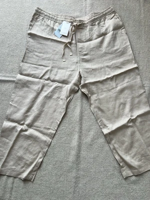 Mango  linnebyxor med dragsko mng - Säljerjer ett par ljusbeige linnebyxor från Mango med avslappnad passform och elastisk midja med dragsko. Tillverkade i 100% linne för en luftig och skön känsla. Perfekta för en chill och stilren look.