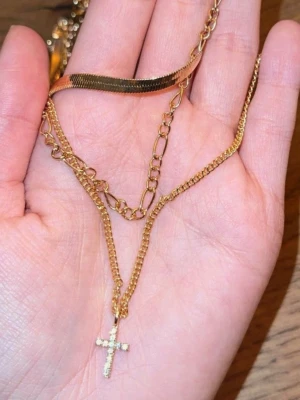 Guldigt lager-på-lager halsband kors - Snyggt guldigt halsband med flera lager kedjor i olika stilar. Det nedersta lagret har ett hängsmycke i form av ett kors dekorerat med små gnistrande stenar. Perfekt för dig som gillar trendiga accessoarer med lite edge.🥹🧸🩷