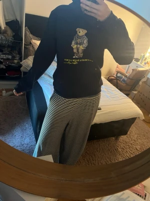 Svart hoodie Polo sopbjörn Ralph Lauren - Svart hoodie från Ralph Lauren med ikoniska Polo Bear- sopbjörnsprintet på bröstet. Klassisk passform med huva de perfekta långa ärmarna. Laidback streetstyle-vibe och riktigt snygg detalj med björnen i cool outfit. Perfekt för dig som vill ha något* extra.