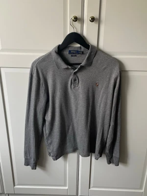 Ralph Lauren långärmad piké  - Klassisk grå långärmad pikétröja från Polo Ralph Lauren i slim fit-modell. Tröjan har krage, knappar vid halsen och den ikoniska broderade loggan på bröstet. Inga defekter. Skriv vid frågor!