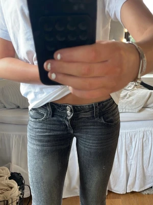 Mörkblå bootcut jeans - Säljer ett par mörkgråa bootcut jeans med snygg slitning på låren och klassiska  fickor. Jeansen har en låg midja och är tillverkade i mjuk denim med lite stretch för extra komfort. Perfekta för en avslappnad och trendig look. Har vuxit ur dom 