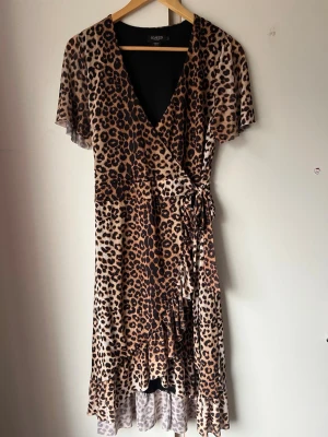 Leopardmönstrad omlottklänning - Säljer en leopardmönstrad omlottklänning från Soaked in Luxury med volangkant och knyt i midjan. Klänningen har korta ärmar och v-ringning, perfekt för dig som vill sticka ut med ett djurmönster. Materialet känns lätt och luftigt.