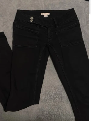 Svarta jeans från Gina Tricot - Säljer ett par svarta jeans från Gina Tricot med raka ben och två stora framfickor. Jeansen har dubbla knappar i midjan och är tillverkade i ett stretchigt material som sitter snyggt. Perfekta för dig som gillar en enkel och stilren look.