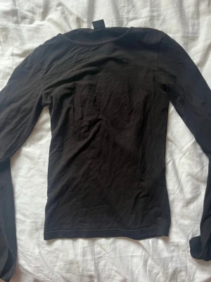Svart långärmad topp med slits i ärmarna - En enkel svart långärmad topp med rund hals. Modellen är tight och passar perfekt till många olika stilar. Tillverkad i mjukt bomullsmaterial som känns skönt mot huden. Perfekt basplagg för garderoben.