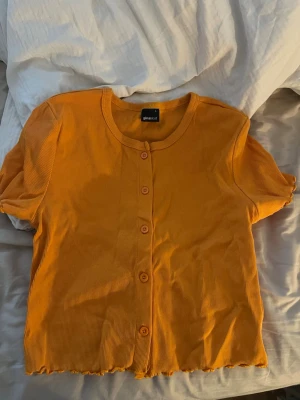 Orange ribbad topp från Gina Tricot - Kortärmad orange ribbad topp från Gina Tricot med knappar framtill.  L men liten i storlek skulle jag säga, passar M.