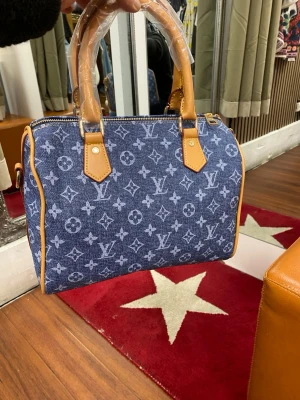 Matcha blå handväska - Snygg handväska  Väskan har ljusbruna läderhandtag och detaljer samt guldfärgade metalldelar. Perfekt storlek för det viktigaste och en ikonisk accessoar till din outfit.