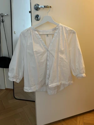 Vit blus med v-ringning från H&M - Säljer en luftig vit blus från H&M med v-ringning och trekvartsärmar. Blusen har en avslappnad passform och är gjord i ett lätt tyg, perfekt för en stilren och enkel look. Passar till både jeans och kjol.