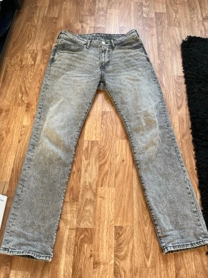 Grå tvättade raka jeans - Säljer ett par grå tvättade jeans med rak passform och klassisk femficksdesign. Jeansen har en snygg vintagekänsla och är tillverkade i denim. Perfekta för dig som gillar en avslappnad och stilren look. Storlek 30/32 köpt på HM. Personen på bilden är 180 cm lång.