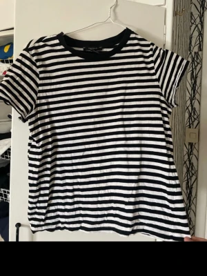 Randig t-shirt från Forever 21 - Säljer en svartvit randig t-shirt från Forever 21. T-shirten har korta ärmar, rund halsringning med svart kant och är gjord i mjuk bomull. Perfekt till jeans eller shorts för en enkel och stilren look.