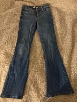 Blå bootcut jeans från Gina Tricot - Säljer ett par klassiska blå bootcut jeans från Gina Tricot då dem är för korta på mig. Jeansen har fickor och normal 'mid rise' passform. Jeansen har utsvängda ben och är gjorda i stretchigt denimtyg för extra komfort. Perfekta för dig som gillar retrovibbar och en avslappnad look.