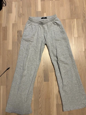 Grå mjukisbyxor med vida ben - Gråa mjukisbyxor med resår i midjan och vida ben. Byxorna har en avslappnad passform och är tillverkade i mjukt bomullsmaterial. Perfekta för en chill och bekväm stil. 