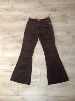 Bootcut Manchesterbyxor - Jättecoola byxor med vida bootcut i brunt manchester. Från märket Smog Rockers. Medelhög midja och långa ben. Midja: 39cm Innerbenslängd: 84cm Byxans längd: 109cm. 