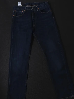 Mörkblå Levi's 501 jeans straight fit - Snygga mörkblå jeans från Levi's med klassisk femficksmodell och raka ben. Jeansen har kontrastsömmaror long och en ikonisk läderpatch bak i midjan. Tillverkade i slitstark denim med en tidlös look som passar till det mesta.