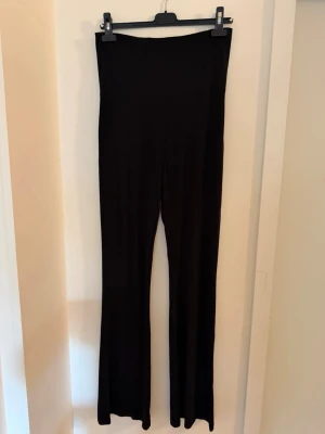 Svarta utsvängda leggings - Svart jersey byxor i mjukt och stretchigt material med hög midja och utsvängda ben. Byxan har en bred linning upptill och har väldigt långa ben och är stor i storleken trots att det stårS på etiketten.. Passar en M.( Den är för lång för mig som är 173cm).