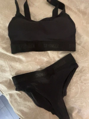 Svart bikini från Stronger - aldrig använd!! Säljer en svart bikini från Stronger med sportig topp och matchande trosa. Båda delarna har elastiska band med logotypen STRONGER. Toppen har justerbara axelband och materialet är stretchigt och bekvämt, perfekt för stranden eller poolen.
