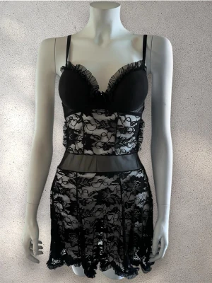 Svart nattelinne med volangdetaljer - Snygg svart nattelinne  i transparent spets med blommönster och volangdetaljer vid kuporna. Justerbara axelband och meshparti i midjan ger en modern look. Perfekt för dig som gillar trendiga och feminina underkläder. #nattelinne 