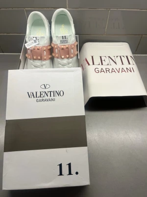 Valentino Garavani Rockstud sneakers - Snygga vita sneakers från Valentino Garavani med rosa band och ikoniska nitar över vristen. Modellen heter Rockstud Untitled och har en chunky sula och klassisk låg silhuett. Tillverkade i läder med coola detaljer som sticker ut.