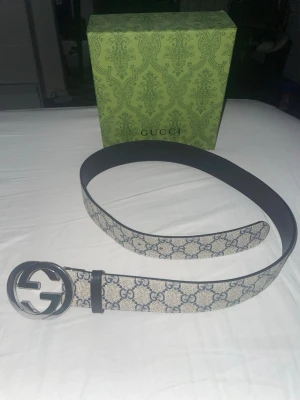  beige bälte med GG-mönster - Snyggt bälte i beige med klassiskt GG-mönster och stor rund metallspänne med logga. Perfekt accessoar för att lyfta din outfit med en lyxig touch. Kommer med originalförpackning.