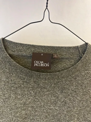Grå stickad tröja från Oscar Jacobson - Snygg grå stickad tröja från Oscar Jacobson med rund halsringning och långa ärmar. Tillverkad i Italien och har en klassisk, stilren design som passar perfekt till jeans eller chinos.