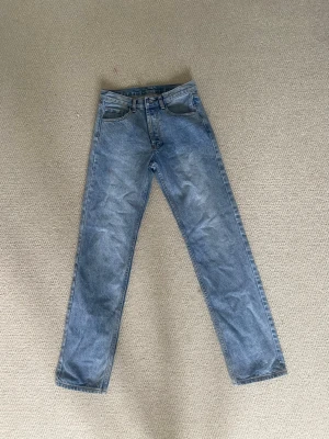 Blå raka jeans i klassisk modell - Säljer ett par ljusblå jeans med rak passform och hög midja. Jeansen har fem fickor och stängs med knappar. Materialet är klassisk denim i bomull och de har en tidlös vintage-look som passar till det mesta. Kom privat för frågor!💕