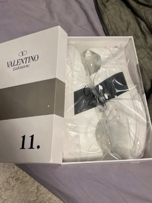 Valentino skor Garavani  - Snygga vita sneakers från Valentino Garavani med svart detalj och logga på sidan. Skorna har en klassisk låg siluett och är tillverkade i läder med vita skosnören. Perfekta för dig som vill ha en stilren och exklusiv look.