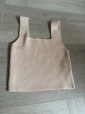 Beige ribbad linnetopp - Snygg beige ribbad linnetopp med breda axelband och fyrkantig halsringning. Perfekt att styla med jeans eller kjol för en trendig look. Mjuk och stretchig känsla som sitter skönt på kroppen.