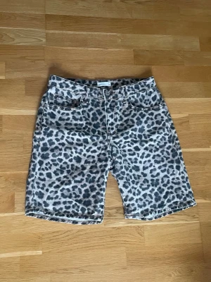 Leopardmönstrade denimshorts - Säljer ett par coola leopardmönstrade shorts i denim med klassisk femficksdesign och knappstängning. De har en midwaist passform och är perfekta för dig som vill sticka ut med ett djurinspirerat mönster. Passar till många olika stilar och är riktigt trendiga. Använda bara någon enstaka gång