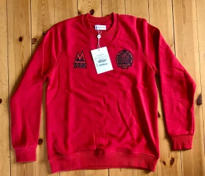 Röd sweatshirt från Moncler 1952 - Snygg röd sweatshirt från Moncler med broderade detaljer framtill, bland annat logga och '1952'. Tröjan har rund halsringning, ribbade muddar och är tillverkad i mjukt bomullsmaterial. Perfekt för en trendig och avslappnad stil.