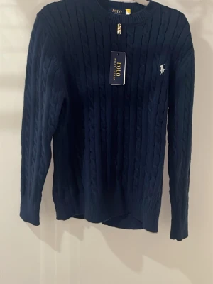 Mörkblå kabelstickad tröja Polo Ralph Lauren - Kabelstickad mörkblå tröja från Polo Ralph Lauren med rund halsringning och klassisk broderad logga på bröstet. Tröjan har långa ärmar och ribbade muddar för en snygg och tidlös look.ny pris runt 1500kr och jag sänker med 60% som är väldigt mycket den är väldigt snygg passar som M så du kan spara den till vintern lovar att den passar. Pris går och diskutera och jag rekommenderar!