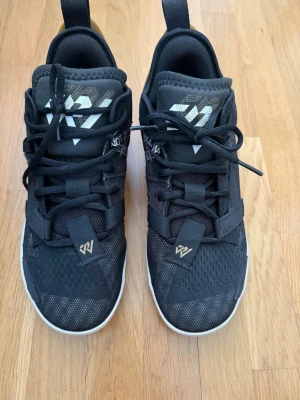 Svarta Jordan Why Not Zer0.4 sneakers - Snygga svarta Jordan Why Not Zer0.4 sneakers med vita och guldiga detaljer. Ovandelen är i mesh och syntetmaterial för bra andningsförmåga. Skorna har vita sulor och coola loggor på plösen och sidan. Perfekta för dig som gillar basketinspirerad stil.