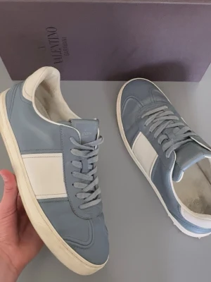 Valentino flycrew - Snygga sneakers från Valentino i ljusblått och vitt läder. Klassisk låg modell med vita detaljer och matchande blå skosnören. Perfekta för dig som vill ha en stilren och trendig look med exklusiv känsla.