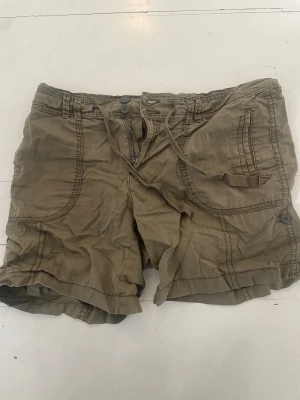 Gröna shorts med snörning från Lindex - Snygga gröna shorts från Lindex med praktiska fickor och snörning i midjan. Perfekta för varma dagar och har en avslappnad passform. Tillverkade i mjuk bomull som känns skön mot huden.