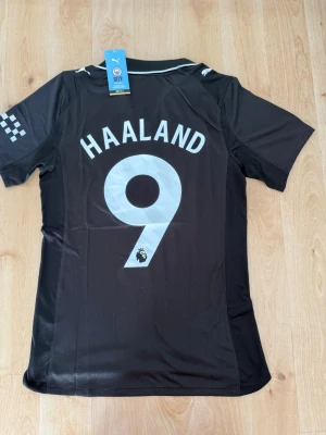 Haaland #9 – Player Edition (storlek M) - Haaland #9-tryck. Player Edition. Storlek M. Helt ny och aldrig använd. Säljs i befintligt skick. Skickas snabbt! 🚚💨  Mått för denna tröja (storlek M): (Uppmätta av leverantör – viss variation kan förekomma) • Halva bröstmåttet: 51 cm • Tröjans längd: 72,5 cm • Ärmbredd: 22,5 cm • Axelbredd: 43 cm • Ärmlängd: 39 cm • Manschettbredd: 18 cm  🔥 Player Edition-modell – tajtare passform än vanliga supportertröjor.