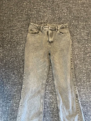 Gråa raka jeans från ZARA - Säljer ett par gråa raka jeans från ZARA med klassisk femficksdesign och hög midja. Jeansen har en snygg tvättad look och stängs med knapp och dragkedja. Perfekta för en avslappnad och trendig stil.