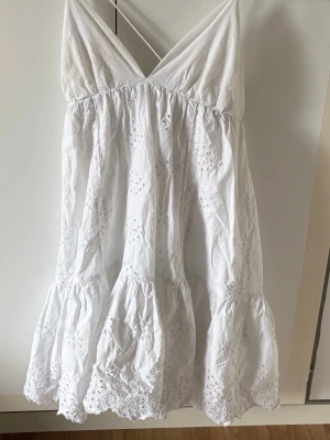 Vit sommarklänning med broderi - Söt vit kortklänning med tunna axelband och v-ringning från Zara. Klänningen har broderade blommönster och volangkant nertill. Perfekt för varma dagar och har en luftig passform. Tillverkad i bomull för en skön känsla. I storlek M men passar S också❤️Har en liten fläck i armhålan men inget man tänker på 