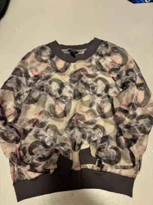 Mönstrad mesh topp med mönster Lindex - Säljer en transparent mesh topp med abstrakt mönster i svart, grått och rosa. Toppen har svarta muddar vid hals, ärmslut och nederkant. Perfekt för dig som gillar statement-plagg och lager på lager.