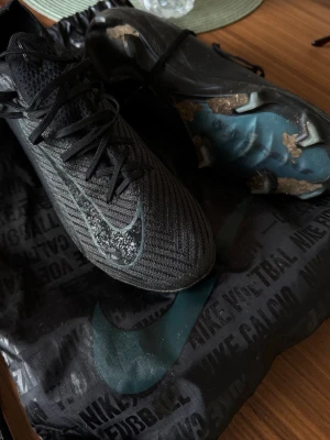 Svarta Nike Mercurial fotbollsskor - Snygga svarta Nike Mercurial fotbollsskor med stickad ovandel och klassisk snörning. Skorna har en diskret Nike-logga på sidan och mönstrad textil för extra grepp. Sulan är designad för bra fäste på gräsplan. Perfekta för dig som vill ha stilrena och snabba skor på planen. Pris går att diskutera! 