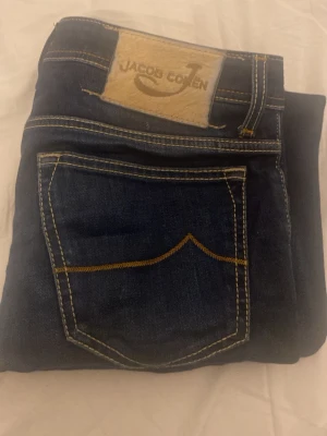 Jacob Cohën jeans - Säljer ett par mörkblå jeans från Jacob Cohen med kontrastsömmar och klassiska bakfickor med broderade detaljer. Jeansen har en snygg passform och är tillverkade i slitstark denim. Perfekta för dig som gillar tidlös och cool stil. Byxorna är i mycket bra. 