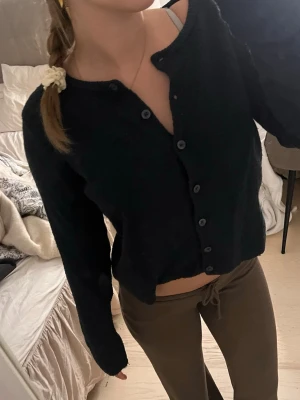 Svart cropped kofta med knappar - Mysig marinblå kofta med långa ärmar och knäppning framtill. Modellen är cropped och har en avslappnad passform, perfekt att styla med höga byxor. Materialet ser mjukt och bekvämt ut, och koftan har en enkel, stilren look.