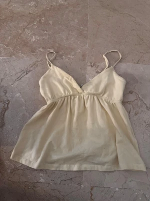 Gul linnetopp från Bershka - Söt ljusgul linnetopp från Bershka med smala axelband och v-ringning. Toppen är tillverkad i mjuk bomull, perfekt för varma dagar.
