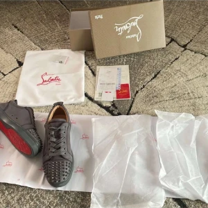 Gråa sneakers med nitar från Christian Louboutin - Säljer ett par gråa sneakers från Christian Louboutin med röd sula! Säljer skorna pga att jag ångrade mitt köp. Skick är 8/10 använda en sommar, kvitto och papper finns med köpet! Helt äkta! Skriv ifall ni är intresserade.