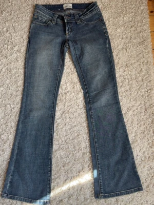 Blå bootcut jeans från Abrand - Snygga blå bootcut jeans från Abrand med klassisk femficksmodell och slitna detaljer. Jeansen har låg midja, bälteshällor och en liten Abrand-logga på bakfickan. Tillverkade i mjuk denim med lätt tvättad look.