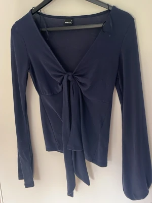Mörkblå långärmad topp med knyt - Snygg mörkblå långärmad topp från Gina tricot  med djup v-ringning och knyt framtill. Tillverkad i mjukt och stretchigt material som sitter skönt på kroppen. Perfekt för dig som gillar stilrena men trendiga plagg.