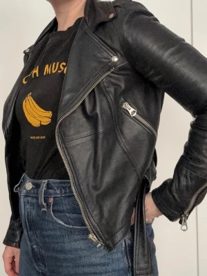 VERAPELLE - Svart skinnjacka med dragkedjor - Cool svart skinnjacka från VERAPELLE med snedställda dragkedjor, axelklaffar och bälte i midjan. Storleken motsvarar S/XS